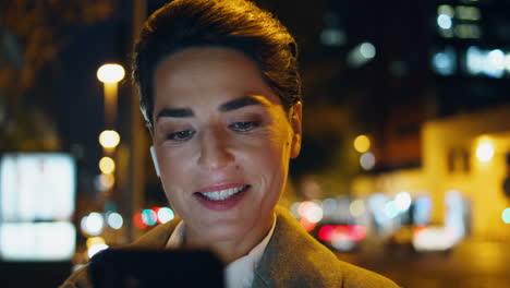 Closeup-happy-woman-surf-smartphone-in-night-city-lights.-Relaxed-manager-look