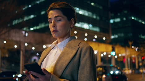 Woman-scrolling-smartphone-night-street.-Successful-late-businesswoman-wait-taxi