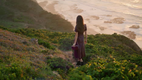 Unknown-woman-walking-hill-near-ocean-holding-book.-Woman-enjoy-evening-coast.