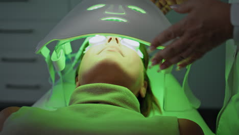 Woman-lying-phototherapy-clinic-close-up.-Beautician-checking-led-light-mask.