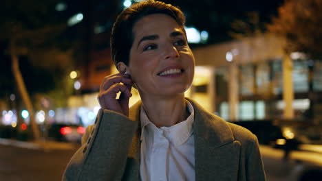 Closeup-night-woman-talking-in-earphones.-Smiling-businesswoman-plug-in-earpods