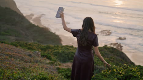 Girl-going-down-coast-to-ocean-holding-book.-Back-view-unknown-girl-walking-hill