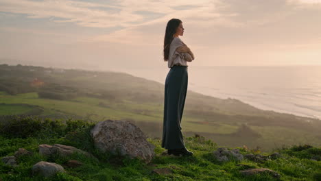 Young-woman-standing-hill-looking-on-seascape-with-sunset.-Model-posing-seacoast