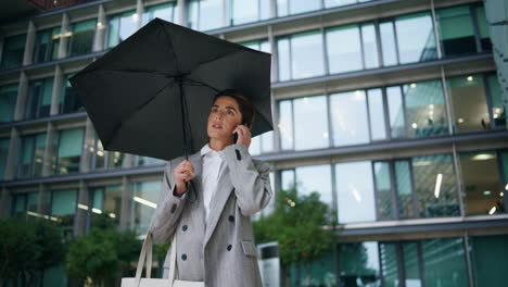 Corporate-woman-talk-mobile-phone-at-contemporary-office-building-on-rainy-day.