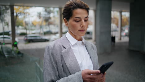 Serious-businesswoman-messaging-smartphone-on-street.-Focused-woman-typing-cell