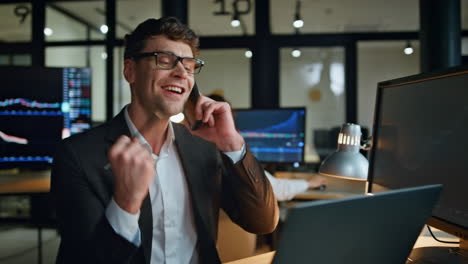 Cheerful-manager-enjoying-call-news-in-evening-workplace.-Stock-happy-man-broker