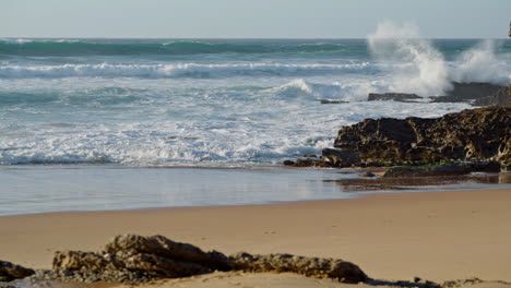 Ocean-crashing-rocky-beach-on-sunny-day.-White-foamy-waves-rolling-coastline