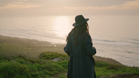 Fashion-woman-posing-sunset-wearing-stylish-hat.-Model-standing-hill-near-ocean.