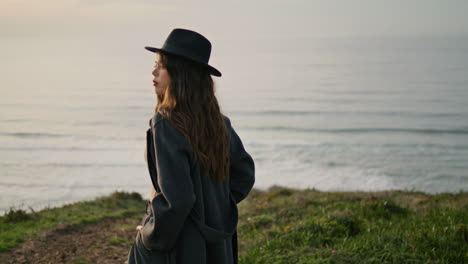 Stylish-girl-looking-sunset-standing-on-green-hill-near-ocean.-Model-posing