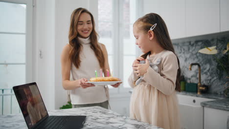 Young-mother-congratulating-daughter-at-kitchen.-Child-looking-at-birthday-cake