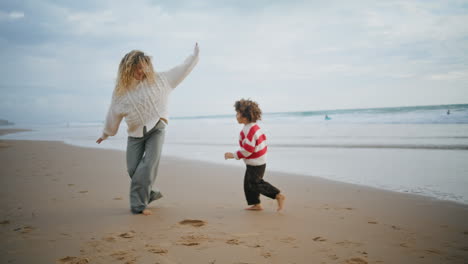 Cute-son-running-mother-on-autumn-seaside.-Happy-babysitter-embracing-child