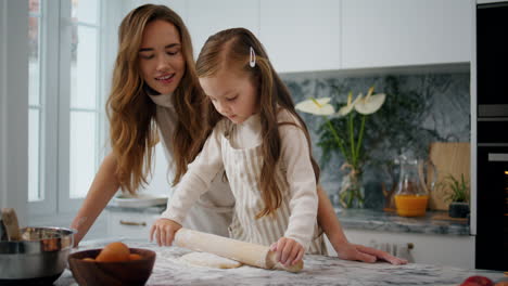 Tender-mother-helping-daughter-at-kitchen-close-up.-Adorable-child-rolling-dough