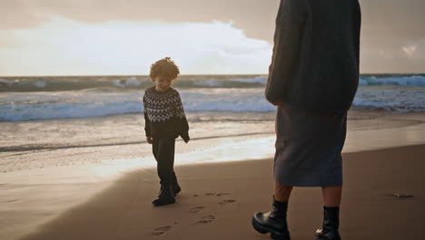 Kid-mother-walking-sand-beach-leaving-footprints-on-sunset.-Joyful-family-play
