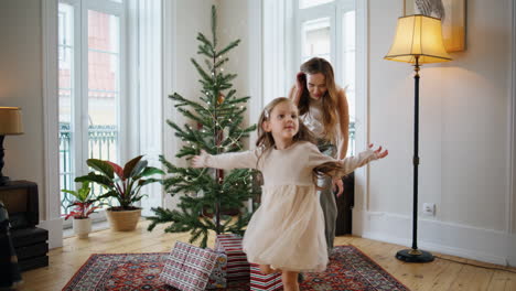 Funny-child-playing-at-Christmas-tree-room.-Smiling-mother-giving-five-daughter