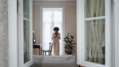 Domestic-girl-open-curtains-at-morning-indoors.-African-woman-enjoying-espresso