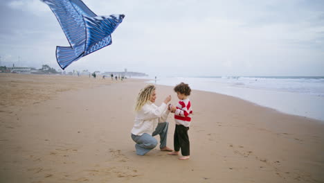 Mom-playing-kite-kid-at-windy-seashore.-Caring-parent-helping-son-launching-toy.