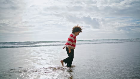 Happy-kid-walking-ocean-water-in-autumn-sunlight.-Joyful-child-playing-waves