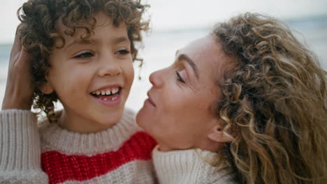 Happy-mother-kissing-son-on-autumn-beach-closeup.-Cute-curly-kid-having-fun