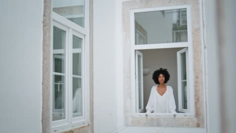 Positive-lady-looking-outdoors-at-window-place.-African-woman-watching-cityscape