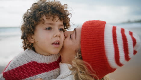 Closeup-mom-cuddling-kid-in-knitted-outfit.-Cute-family-resting-weekend-on-beach