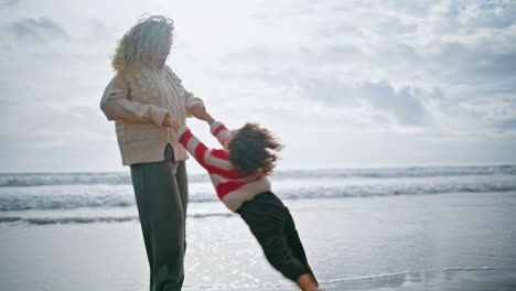 Laughing-parent-spinning-kid-on-spring-ocean-beach.-Joyful-curly-boy-having-fun