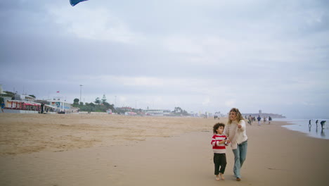 Happy-mother-launching-kite-toy-with-adorable-son-on-autumn-beach-together.