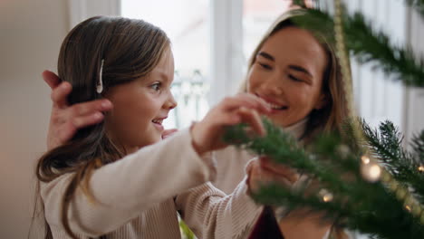 Cute-child-decorating-Xmas-tree-with-mom-home-closeup.-Mother-embracing-daughter