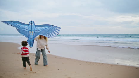 Smiling-mom-playing-kite-with-child-on-seaside.-Joyful-parent-launching-toy