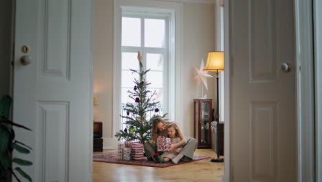 Adorable-family-unpacking-gifts-near-xmas-tree.-Tender-woman-embracing-child