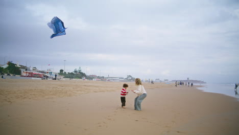 Little-son-playing-kite-with-parent-on-beach.-Joyful-mother-helping-teach-child