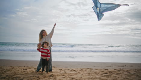 Parent-child-playing-kite-on-ocean-beach-weekend.-Young-single-mom-helping-son