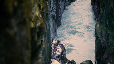 Waves-breaking-at-ocean-cliff-surface-closeup.-Sea-foaming-between-rocks-nature