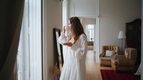 Calm-woman-drinking-tea-at-morning-home-interior.-Tender-lady-watching-window