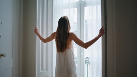 Tender-lady-opening-shutters-at-bedroom.-Relaxed-woman-enjoying-morning-alone
