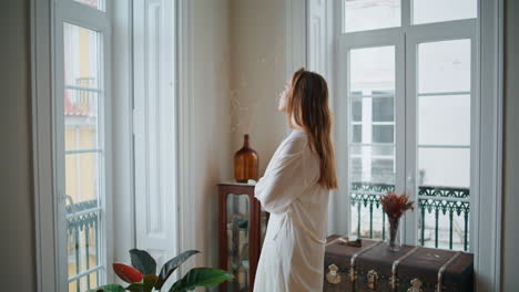 Thoughtful-woman-looking-window-at-light-interior.-Lady-stretching-hands-resting