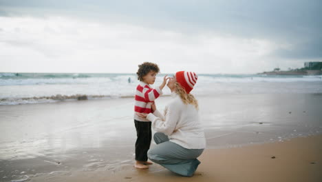 Mom-son-resting-seaside-on-autumn-weekend.-Adorable-little-boy-touching-mother