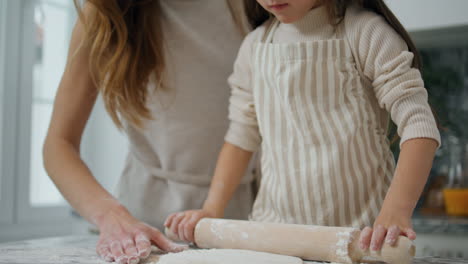 Mother-daughter-rolling-dough-home-close-up.-Smiling-woman-teaching-kid-cooking