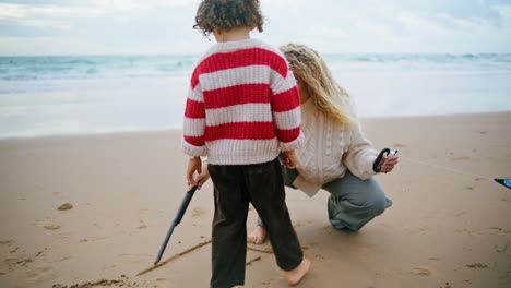 Mother-son-drawing-beach-with-sticks-on-autumn-weekend.-Family-playing-seaside