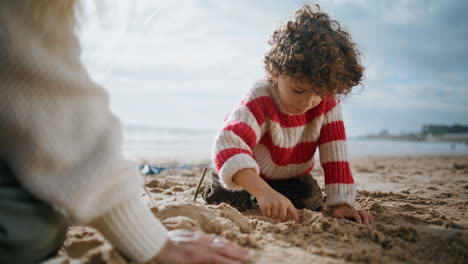 Cute-boy-building-sand-figures-at-ocean-shore.-Focused-curly-child-rest-outdoors