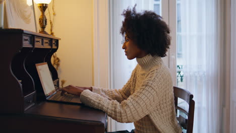 Una-Mujer-Seria-Trabaja-Con-La-Computadora-En-Una-Mesa-Vintage.-Freelancer-Africano-Escribiendo-Portátil