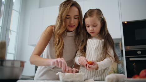 Curious-daughter-decorating-cake-with-mom-kitchen-closeup.-Woman-teach-kid-bake