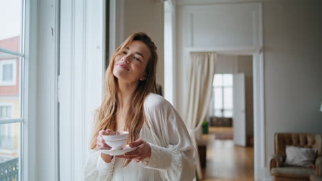 Positive-girl-drinking-tea-home-portrait.-Smiling-woman-posing-camera-at-house