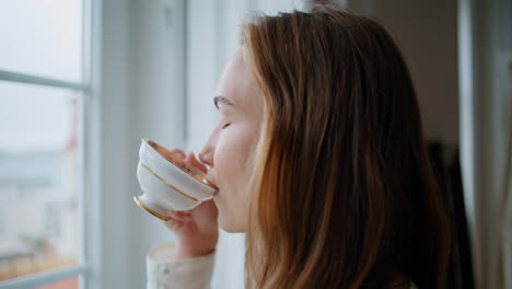 Woman-hands-holding-tea-cup-window-place-closeup.-Satisfied-lady-sniffing-coffee