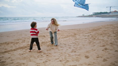 Kid-trying-launching-kite-with-mom-on-windy-beach.-Excited-mother-helping-son