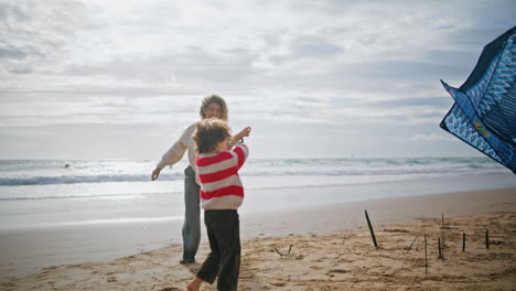 Mother-son-launching-kite-on-windy-ocean-shore.-Cheerful-woman-helping-child