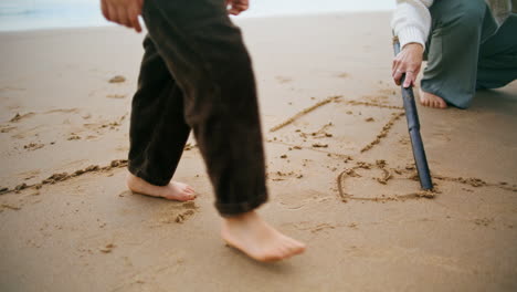 Closeup-hand-draw-beach-sand-on-family-weekend.-Unknown-boy-legs-walking-seaside