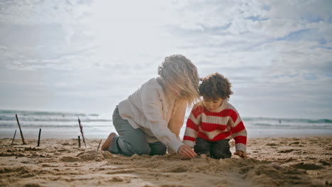 Mother-relaxing-autumn-beach-with-little-son.-Carefree-family-building-sand