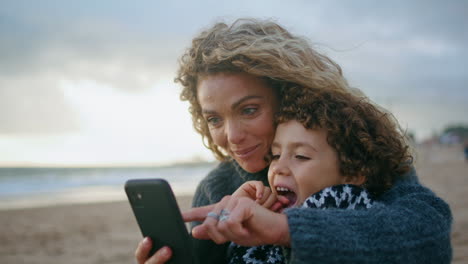 Closeup-family-taking-selfie-on-cloudy-beach.-Beautiful-young-mother-hugging-son