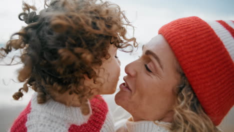 Happy-child-kissing-mom-having-fun-together-at-ocean-shore-together-closeup.