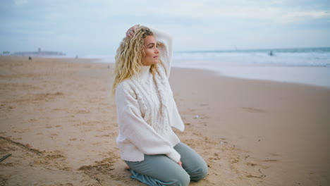 Woman-resting-autumn-beach-on-cloudy-day.-Beautiful-curly-tourist-looking-camera